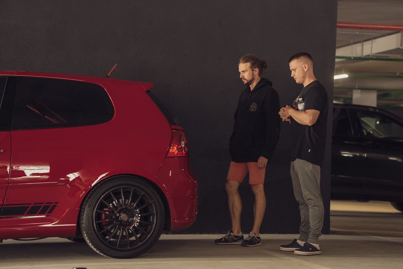 Serhii Shramko and a friend examining the rear of a red sporty car in a parking garage