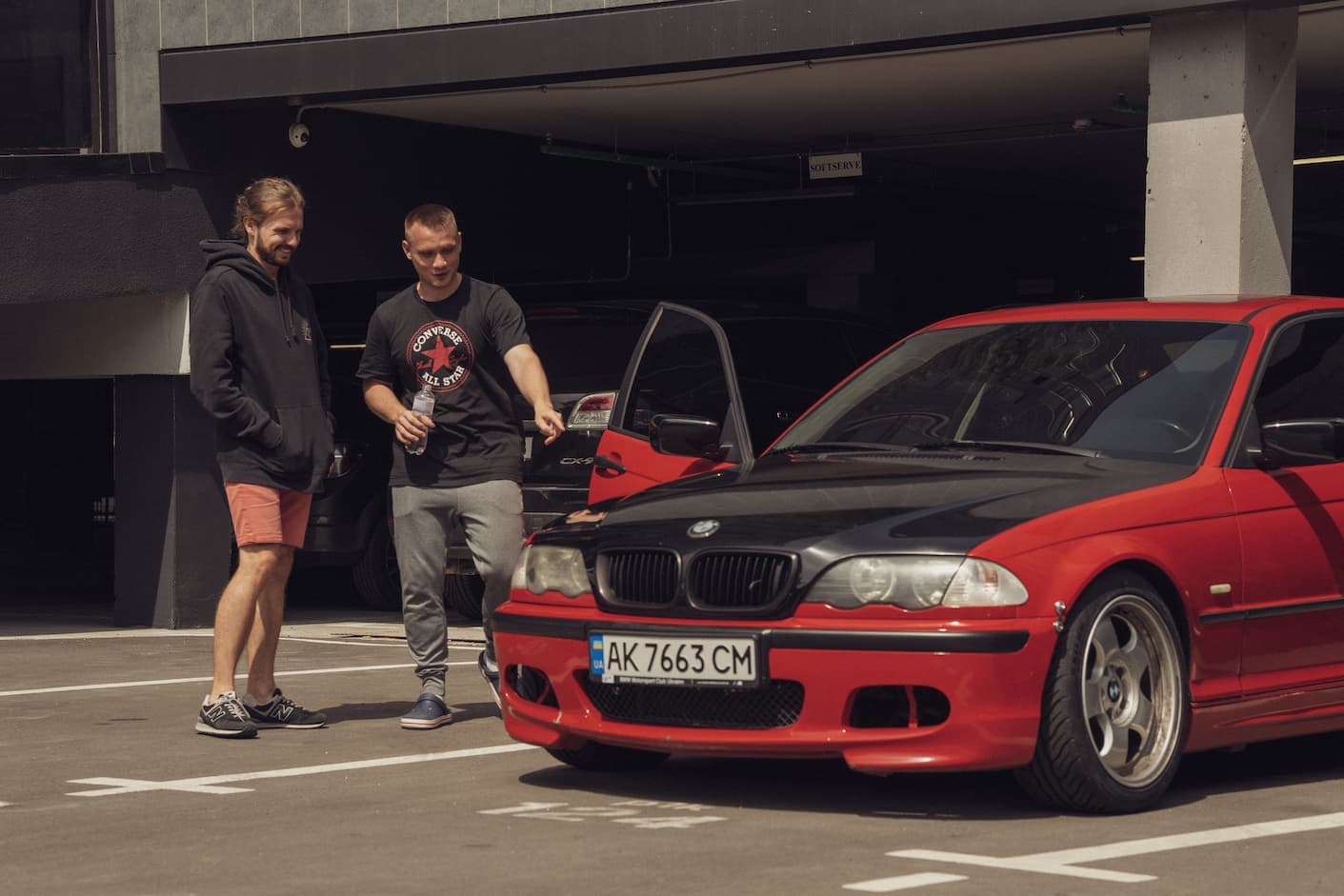 Serhii Shramko showing a red and black BMW to a friend in an outdoor parking lot.